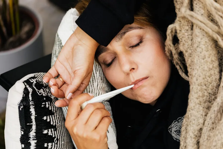Woman checking her temperature with a thermometer, sweating at night when sick